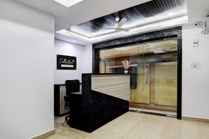 A reception area with a black reception desk, a ceiling fan, and a glass door leading to another room. - Classic With Twin Bed Victoria Inn (Barasat)