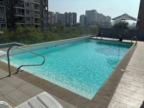 A swimming pool with a metal ladder, surrounded by a tiled deck, and a cityscape in the background. - Modern and spacious shelter steps away from Plaza Ñuñoa (Ñuñoa)