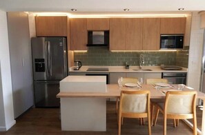 A modern kitchen with wooden cabinets, stainless steel appliances, a central island, and a dining area with wicker chairs. - Modern and spacious shelter steps away from Plaza Ñuñoa (Ñuñoa)