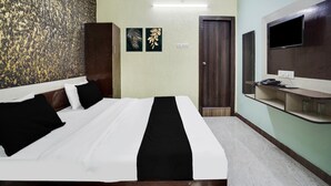 A hotel room with a bed, a television, a desk, and artwork on the wall. - Deluxe Royal Stay Inn (Prayagraj)