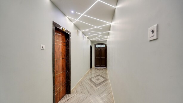 A hallway with a wooden door, a patterned floor, and recessed lighting. - Deluxe Royal Stay Inn (Prayagraj)