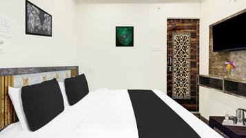 A hotel room with a bed, a TV, a decorative wall panel, and a small table with a kettle.