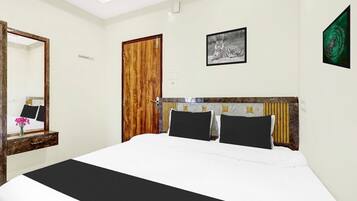 A hotel room with a bed, a wooden door, a framed picture, and a mirror.