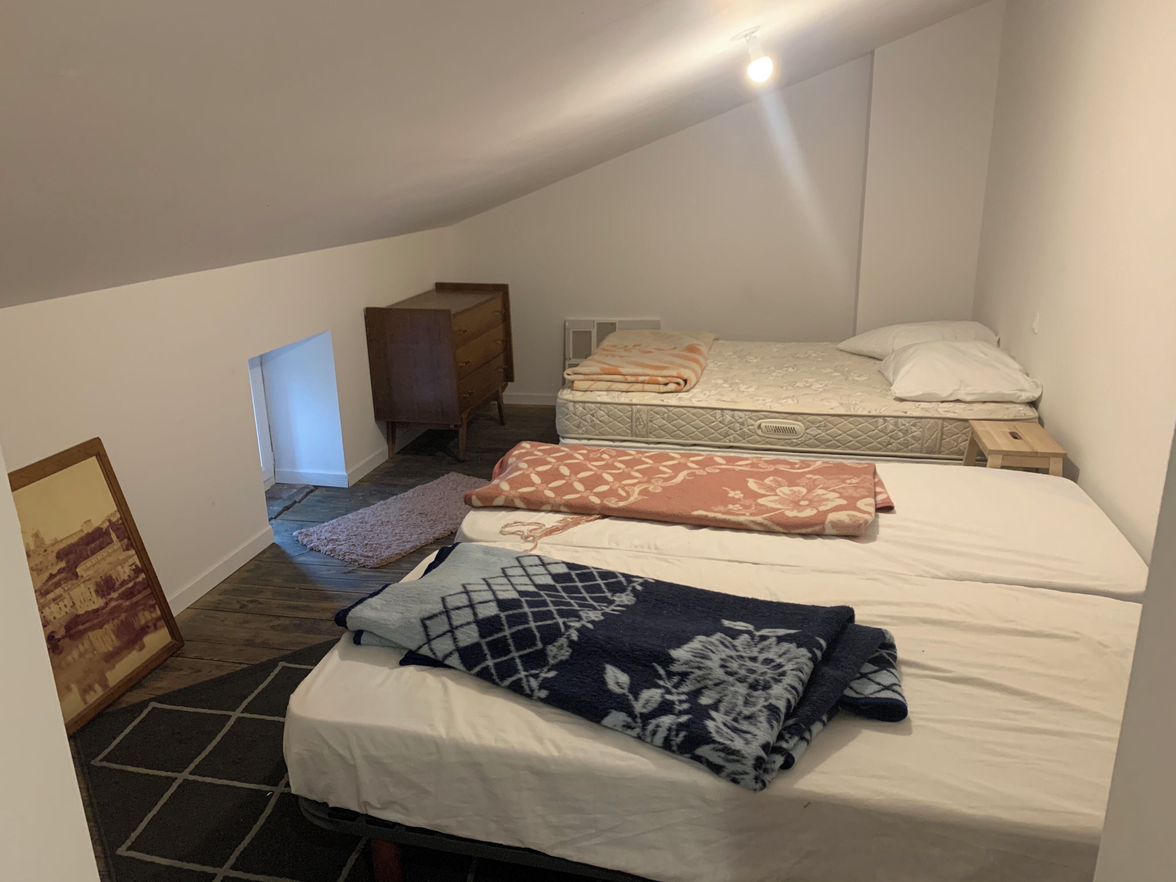 A dorm-style room with two beds, a dresser, and a small desk.