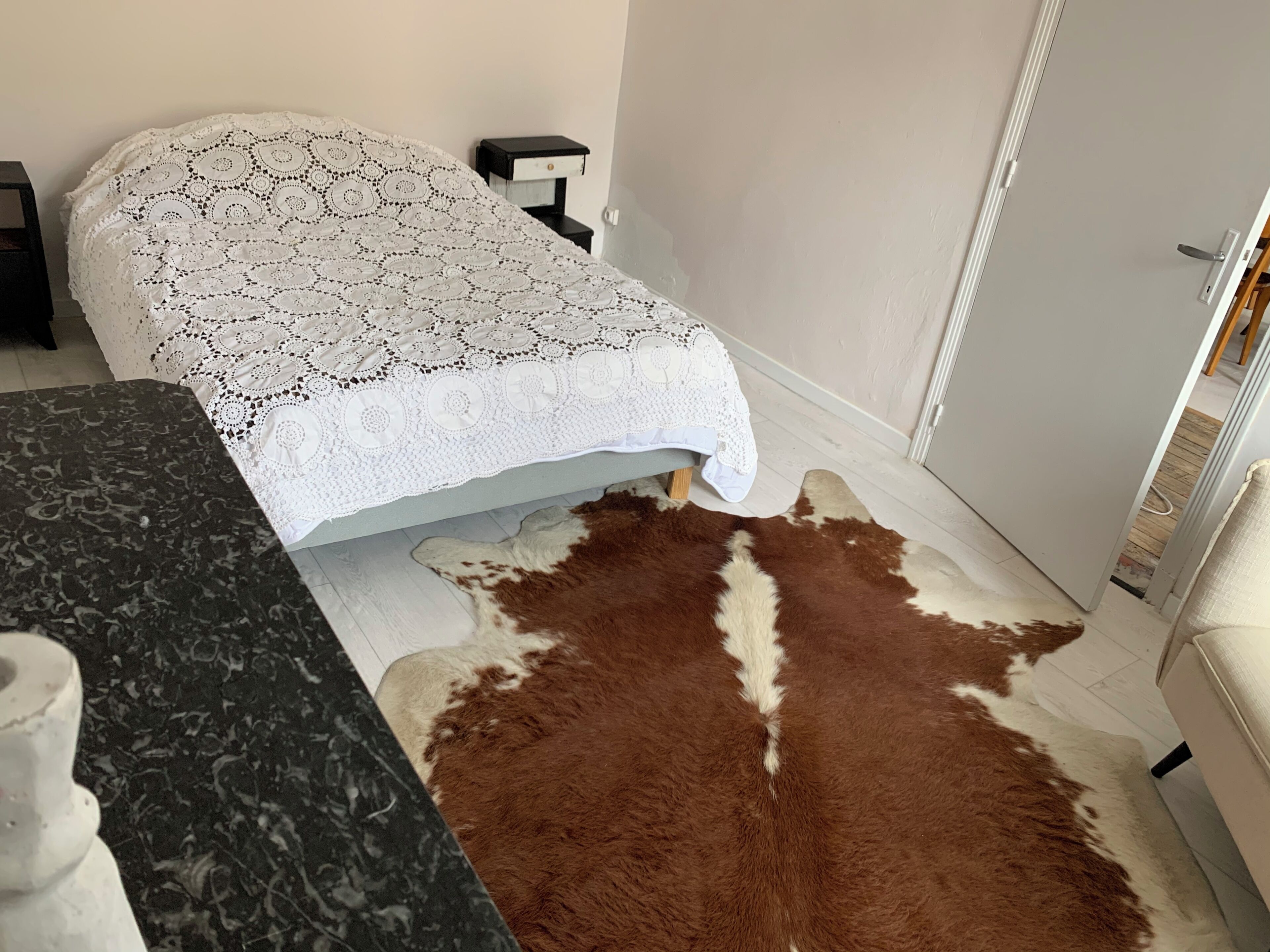 Una habitación con una cama, una mesita de noche pequeña, un tapete de cuero de vaca y una encimera de mármol.
