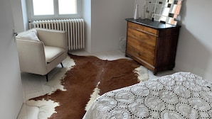 A room with a radiator, a wooden dresser, a cowhide rug, and a bed with a patterned bedspread.
