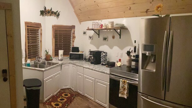 Una cocina con armarios blancos, microondas, estufa, refrigerador y techo de madera.