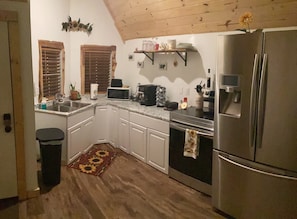 A kitchen with white cabinets, a microwave, a stove, a refrigerator, and a wooden ceiling.