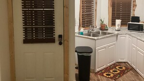 Una cocina con armarios de madera, un lavamanos, un microondas y una puerta con persianas.