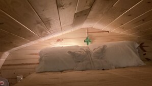 Techo de madera con techo inclinado, una cama con ropa blanca y un enchufe visible.