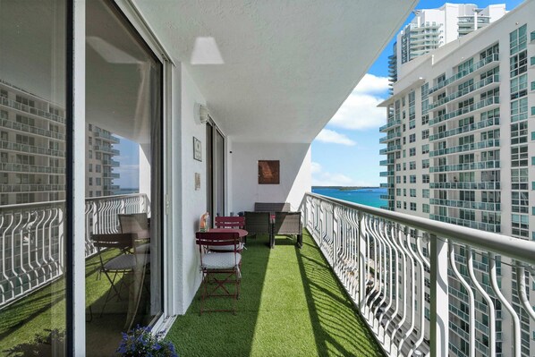 A balcony with a view of the ocean, furnished with chairs and a table, and surrounded by white railings. - Plush Brickell 1BR | Free Parking | Resort Pool (Brickell)