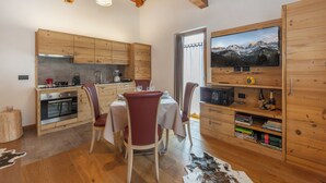 A wooden interior with a kitchen, dining area, and a mounted TV displaying a mountain scene. - Apt "Homewood": rustic design with park and biolago (Pinzolo)