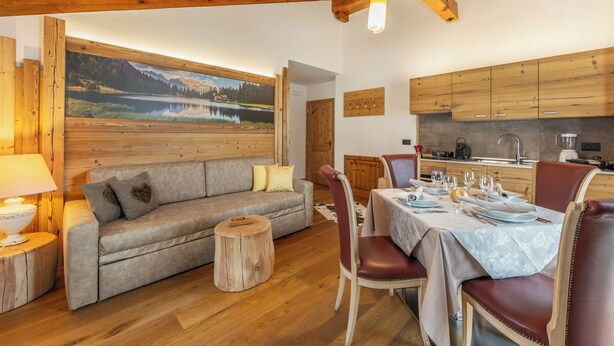 A cozy room with a wooden ceiling, a sofa, a dining table set for four, and a kitchen area. - Apt "Homewood": rustic design with park and biolago (Pinzolo)