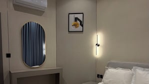 Une chambre d’hôtel avec un lit, un appareil de climatisation, un miroir rond, un tableau encadré et une table de chevet.