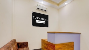 A reception area with a sign reading 'TOWNHOUSE Company Service,' a wooden reception desk, and a brown leather couch. - Deluxe Zafe Commercial (Chengalpattu)