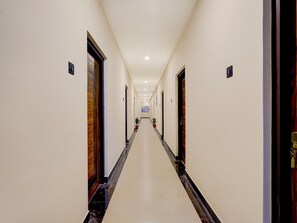 A long, narrow hotel corridor with doors on both sides, a tiled floor, and a ceiling with recessed lighting.