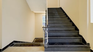 A staircase with black steps leading to a landing, white walls, and a small window at the top. - Deluxe Zafe Commercial (Chengalpattu)