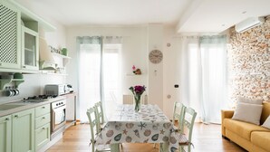 Uma cozinha com fogão, forno e armários, uma mesa de jantar com cadeiras, um sofá e uma parede com padrão de tijolos.