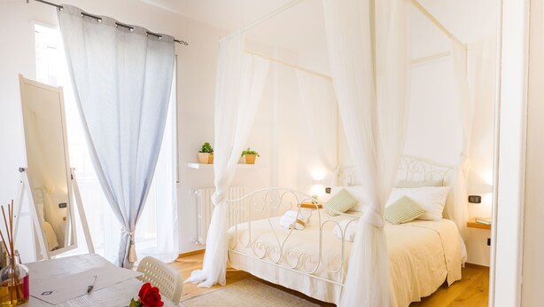 Quarto com cama de dossel, mesas de cabeceira, abajur e janela com cortinas.