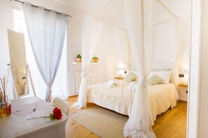 Ein Schlafzimmer mit einem Himmelbett, Nachttischen, einer Nachttischlampe und einem Fenster mit Vorhängen.