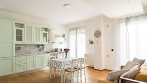 Uma cozinha com mesa de jantar, cadeiras e um sofá numa sala de estar iluminada.