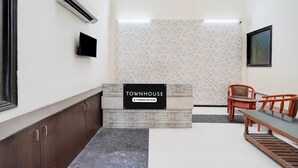 A reception desk with a sign reading 'TOWNHOUSE Company Serviced,' a flat-screen TV, a wall-mounted air conditioner, and a seating area with a table and chairs. - Townhouse Sector 51 Noida (Noida)