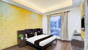 A modern hotel room with a large bed, a bedside table with a plant, a TV, and a view of the city. - Townhouse Sector 51 Noida (Noida)