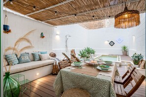 An outdoor dining area with a table set for two, a wooden bench, a hanging light fixture, and a white brick wall. - Dimora Sardaro - Suite with Pool by BarbarHouse (Monopoli)