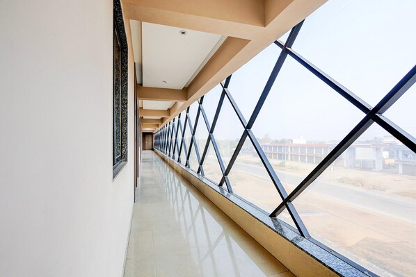 A corridor with a reflective floor, a series of windows with a geometric pattern, and a view of a road and buildings outside.