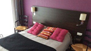 Ein Bett mit dunklem Kopfteil, zwei Wandlampen und ein Fenster mit Vorhängen.
