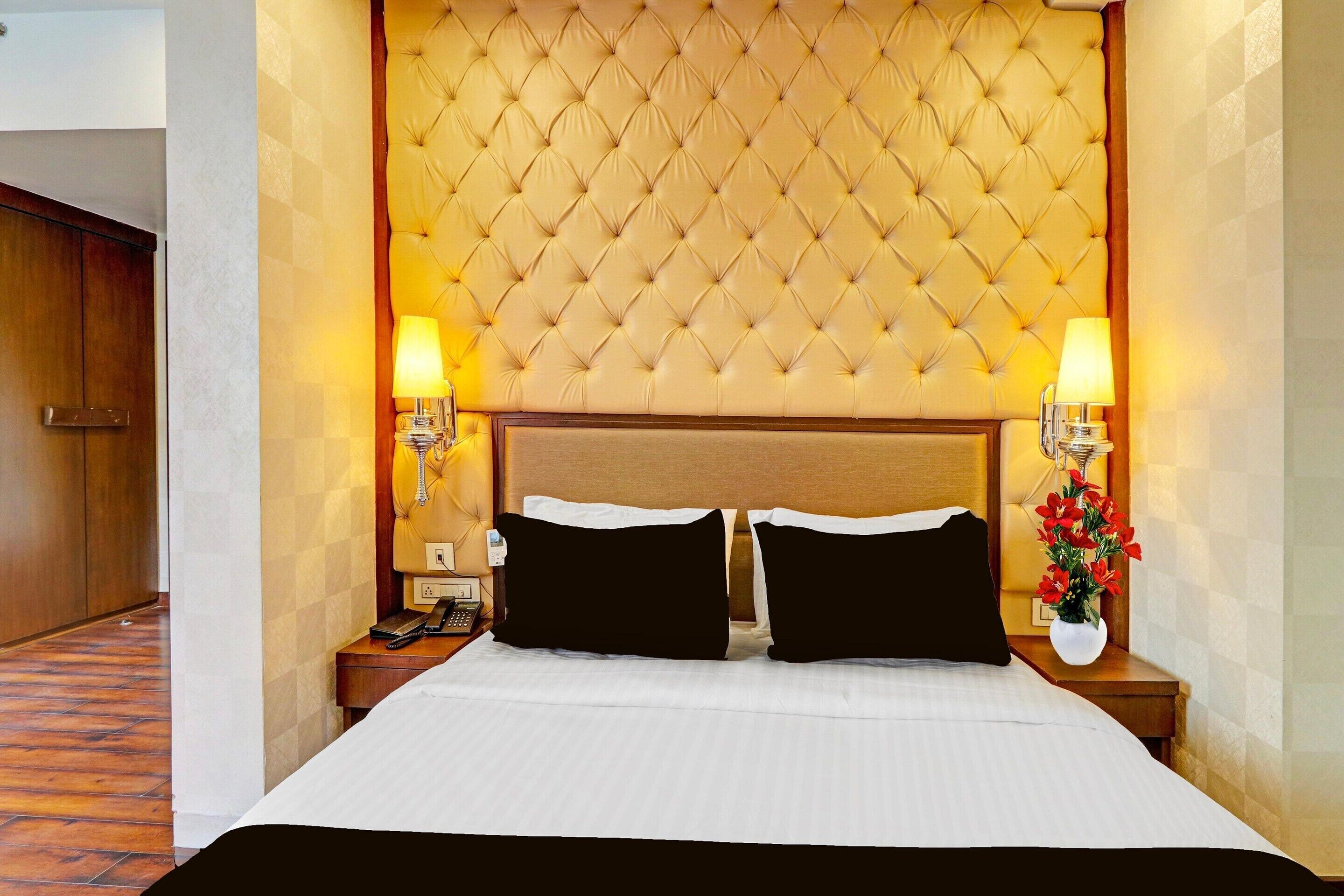 A hotel room with a tufted headboard, two bedside lamps, a telephone, and a vase with flowers.