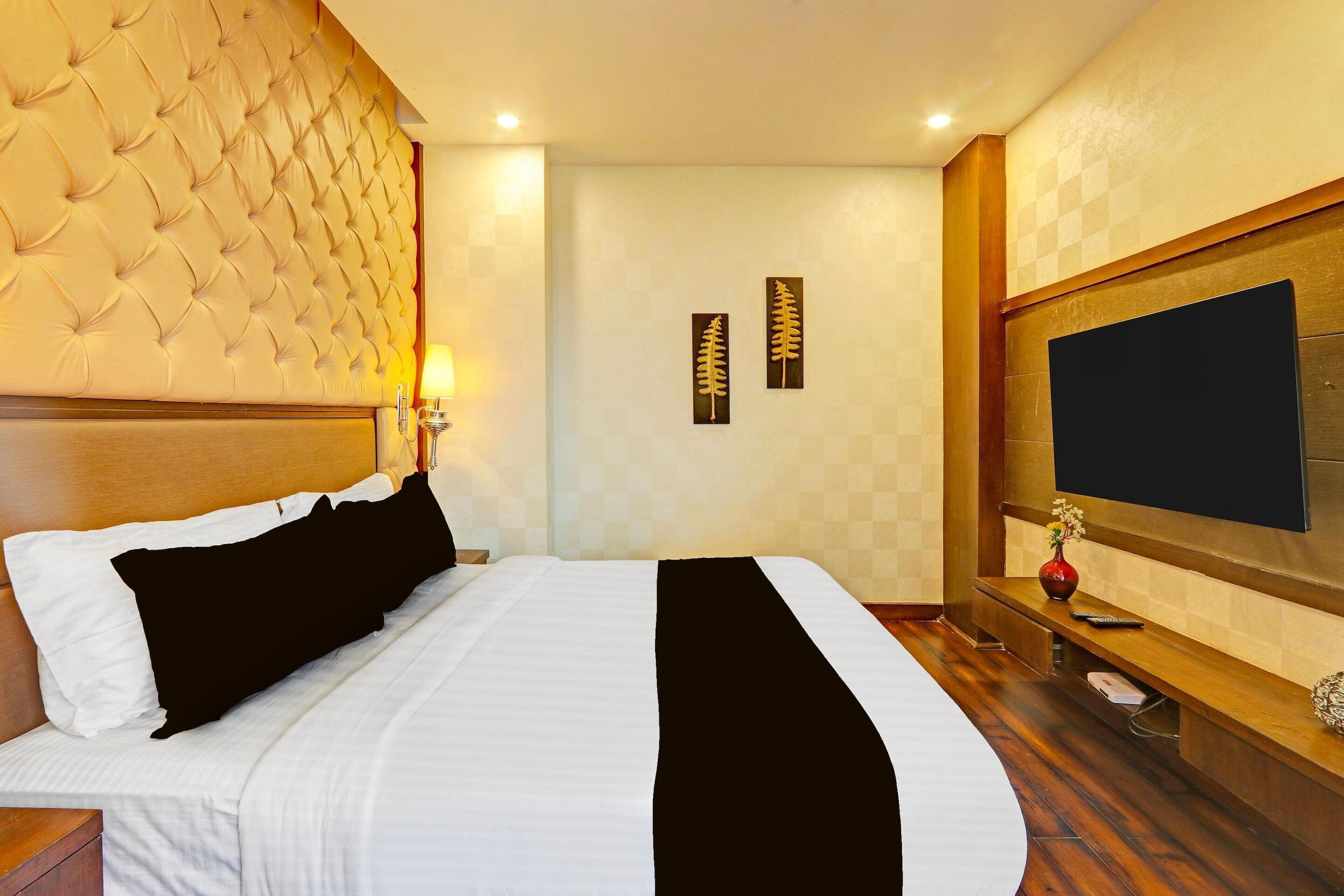Hotelkamer met een gestuufd hoofdeinde, een bed met zwart-witte beddengoed, een flatscreen televisie aan de muur en een tafeltje met een vaas en afstandsbedieningen.