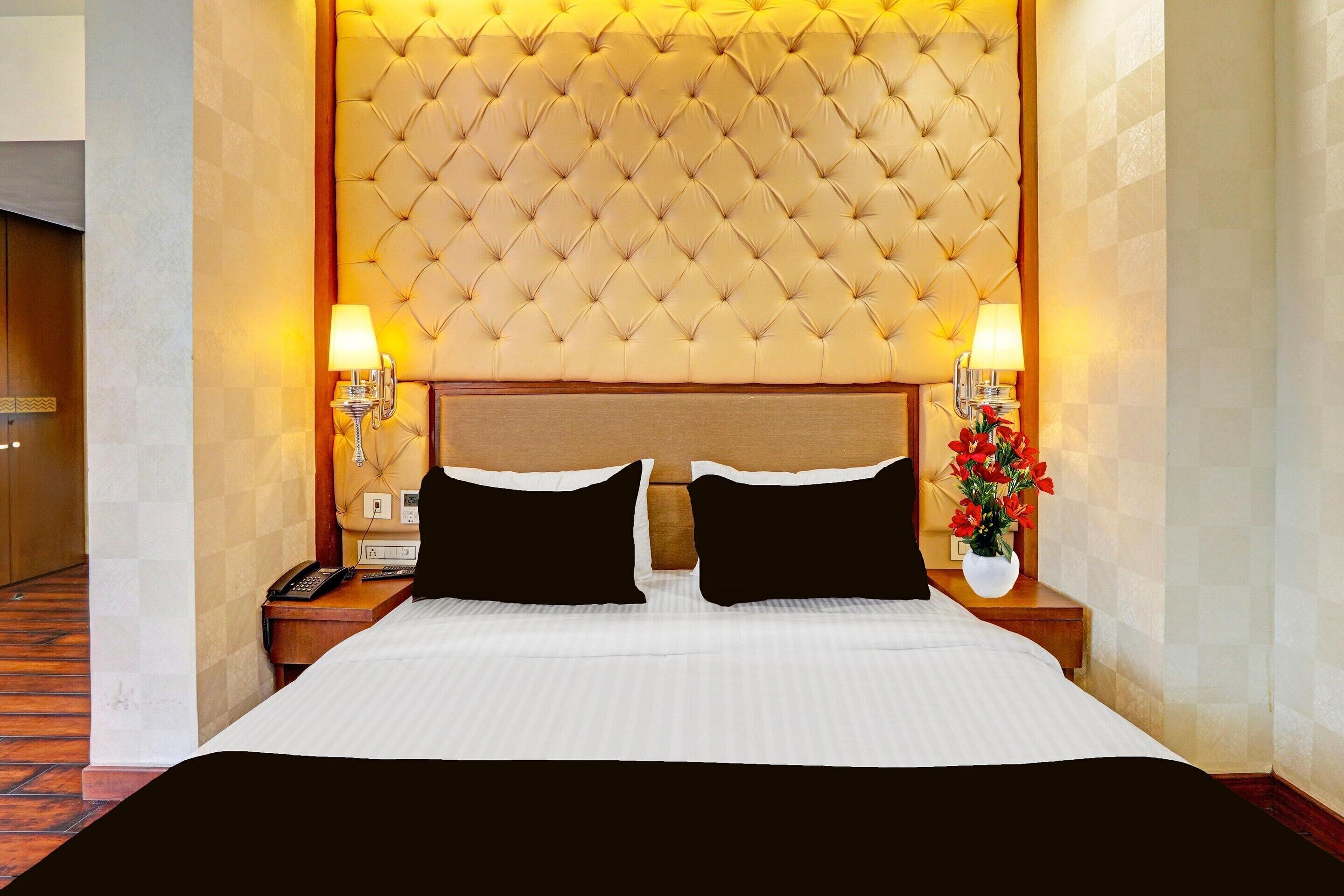 Une chambre d’hôtel avec un grand lit, une tête de lit capitonnée, des lampes de chevet et un vase rempli de fleurs.