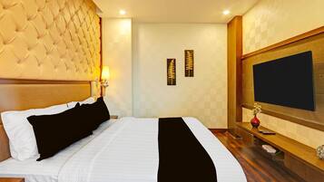 A hotel room with a tufted headboard, a flat-screen TV, a bedside table with a vase, and two wall-mounted picture frames.