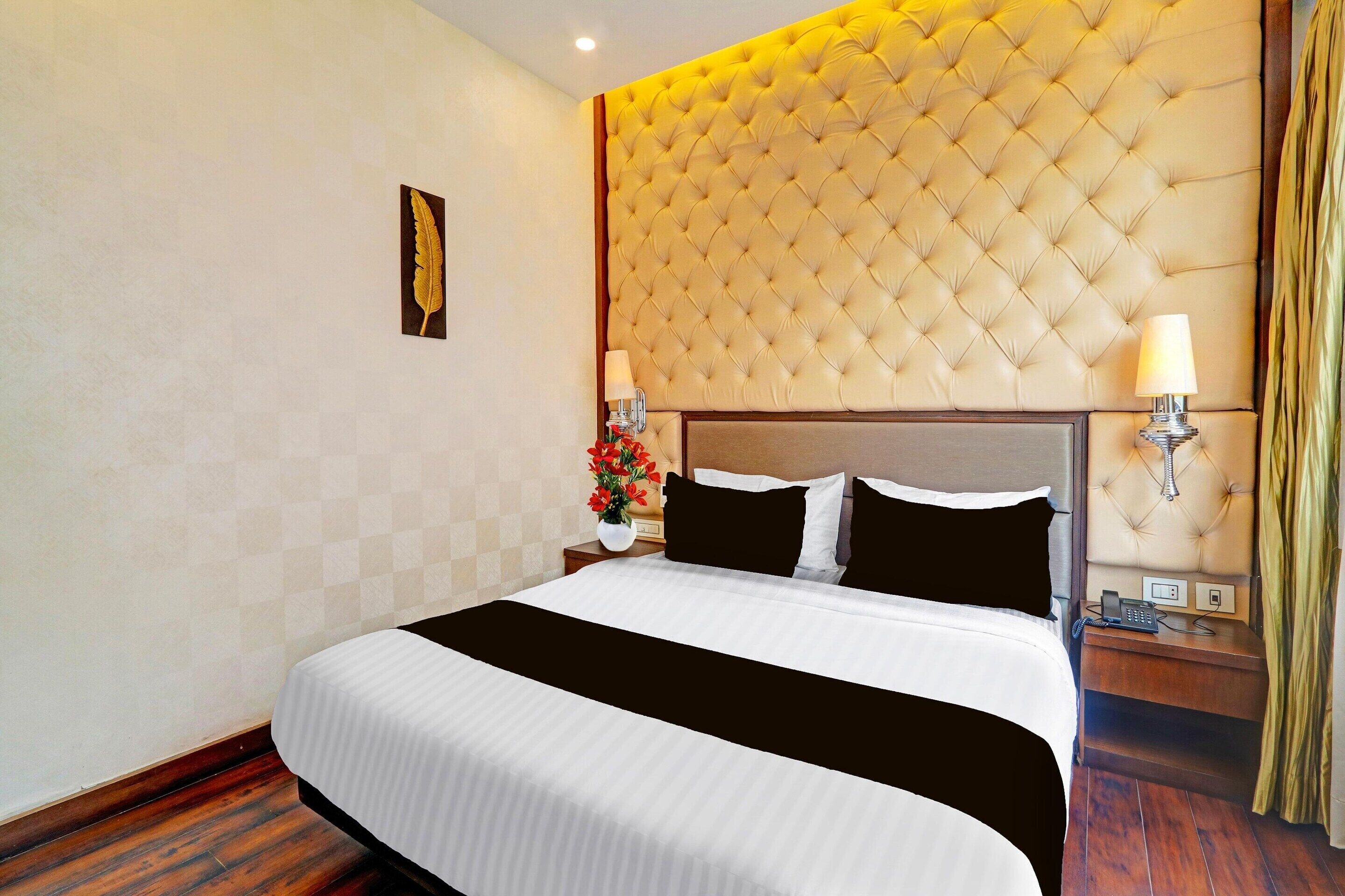 A hotel room with a large bed, a tufted headboard, a nightstand with a lamp, and a wall-mounted telephone.