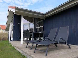 Et overdækket udendørs område med et bord, stole og en terrasse, samt udsigt til huset.