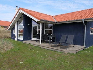 Et hus med rødt tegltag, en overdækket terrasse med et bord og stole, og en mørkeblå facade.