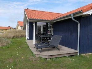 Et hus med røde tegltag, en overdækket terrasse med stole og en mørkeblå facade.