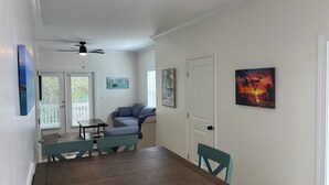 Uma área de refeições com mesa e cadeiras de madeira, um ventilador de teto e obras de arte nas paredes.