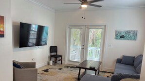 Sala de estar com televisão de tela plana, ventilador de teto, mesa de jantar e sofá.