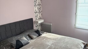 Une chambre à coucher comprenant un lit, une tête de lit, un climatiseur fixé au mur, une fenêtre avec des stores et un panneau décoratif mural.