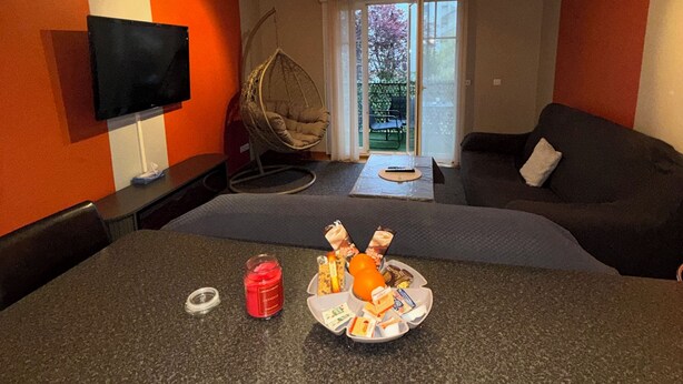 Un salon moderne doté d’un téléviseur à écran plat, d’un canapé, d’une table à manger avec des collations et d’une grande fenêtre.