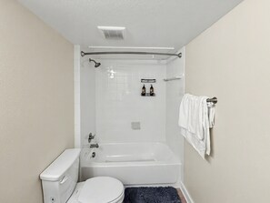A bathroom with a toilet, bathtub, shower, and a towel rack. - The Arlington Suite! (Grand Prairie)