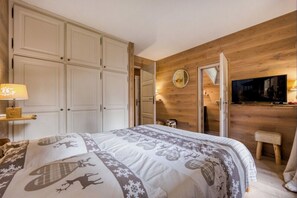 Ein Schlafzimmer mit einem Bett, einem Fernseher, einer Holzwand, einem Kleiderschrank und einem Spiegel.