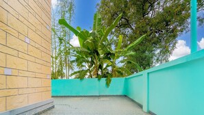 A courtyard with a tiled floor, a brick wall, and a green wall with a banana tree. - Deluxecrystal inn (Coimbatore)