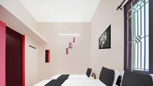 A modern hotel room with a large bed, a red door, a window with bars, and a framed picture on the wall. - Deluxecrystal inn (Coimbatore)