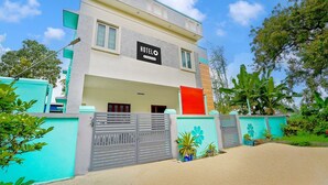 A modern hotel with a sign reading 'HOTELO,' featuring a flat roof, large windows, and a gated entrance. - Deluxecrystal inn (Coimbatore)