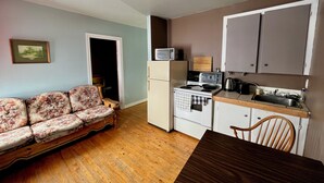 A compact kitchen with a refrigerator, stove, microwave, and wooden dining table. - Bennett Lodge (Daniel's Harbour)
