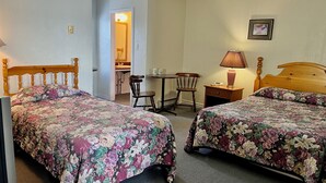 A bedroom with two wooden beds, a desk, a chair, a lamp, and a bathroom visible in the background. - Bennett Lodge (Daniel's Harbour)