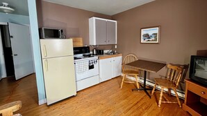 A compact kitchen with a refrigerator, stove, microwave, and cabinets. There is a dining table with two chairs and a television. - Bennett Lodge (Daniel's Harbour)